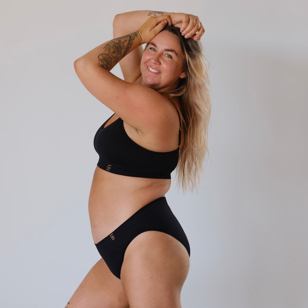 Ethically made recycled seam free black bikini brief by Underwear for Humanity: Flexible and comfortable, stretches across sizes. Models wear bikini brief underwear. Underwear is made from recycled nylon and sits low on the waist, full seat coverage and smooth on the body.