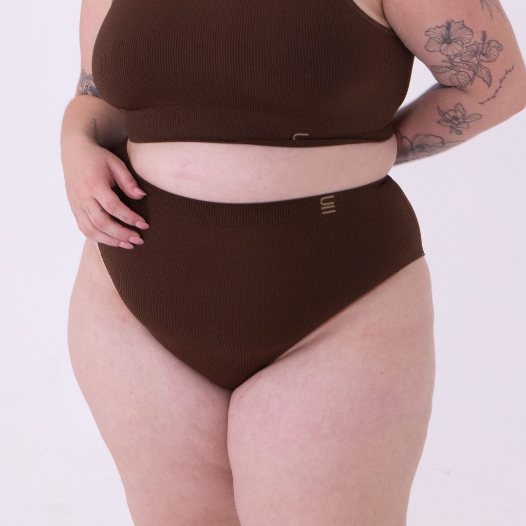 Sustainable nude 6- dark skin tone featured on light skin, seam free high waist brief by Underwear for Humanity: ethical, sustainable. sizes 6-26. light, breathable, stretches across sizes. Models wear high-waisted underwear. underwear sits high on the waist, full seat coverage, Seam free underwear. made from recycled nylon