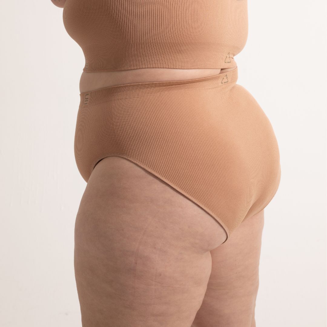 Sustainable, ethically made nude 3 - light beige skin tone, high waist seam free g-string by Underwear for Humanity: Flexible and comfortable, stretches across sizes. Models wear high-waisted G -string underwear. Underwear sits high on the waist, high on the seat, and smooth on the body, made from recycled nylon.