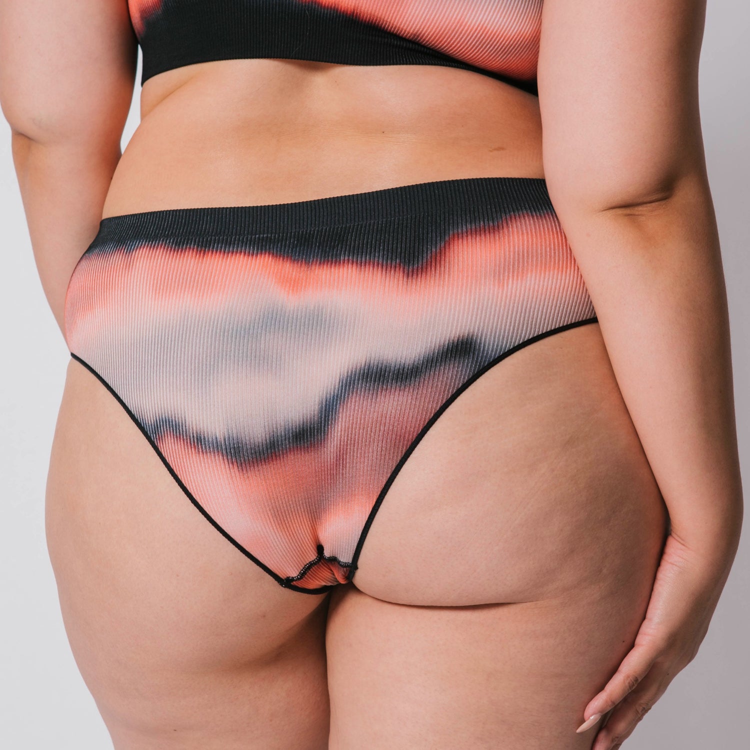 Underwear for Humanity, sustainable, organic and ethically made gradient underwear.  Soft , breathable, Cheeky coverage, sits high on hips. Model wears cheeky underwear in flame, recycled nylon elastic waist band.