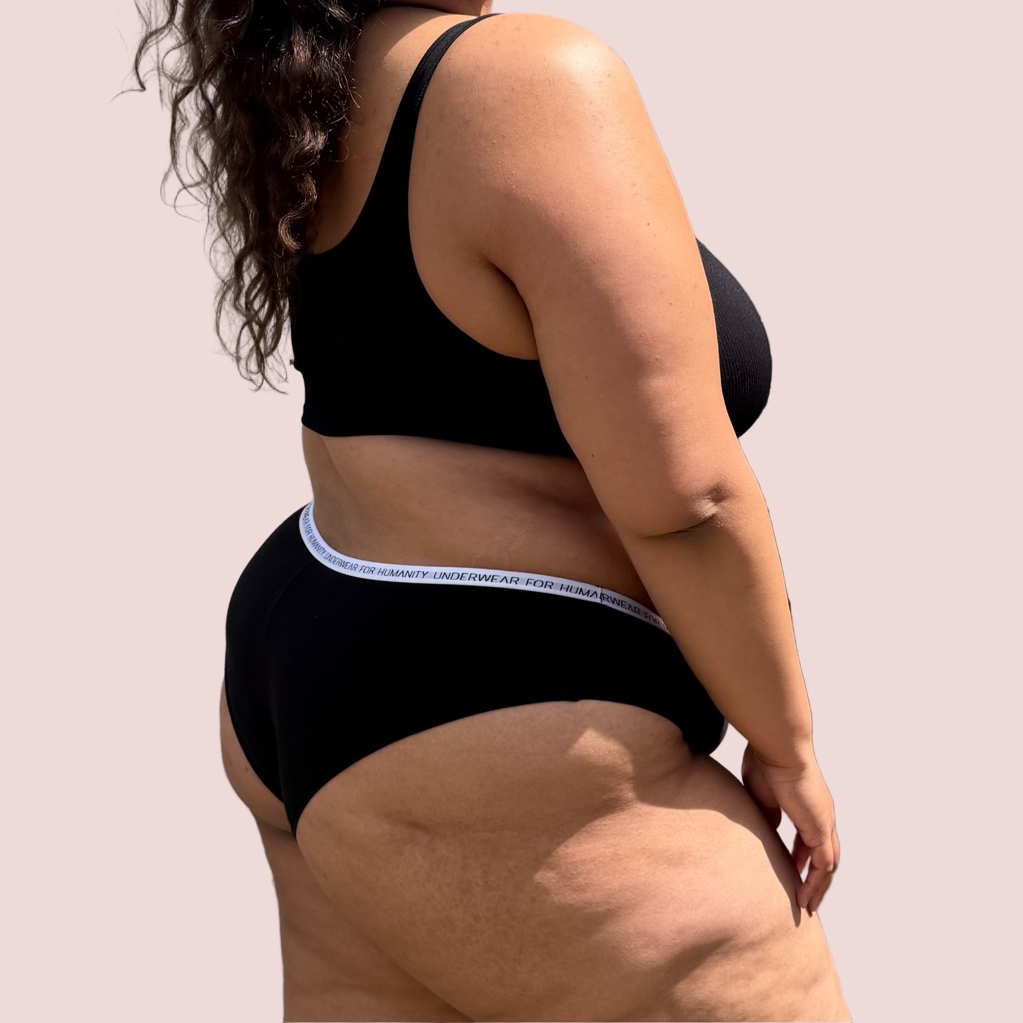 Underwear for Humanity, sustainable, organic and ethically made black cotton underwear. Soft , breathable, Cheeky coverage, sits high on hips. Model wears Cheeky Cotton underwear in black with a white, recycled nylon elastic waist band.