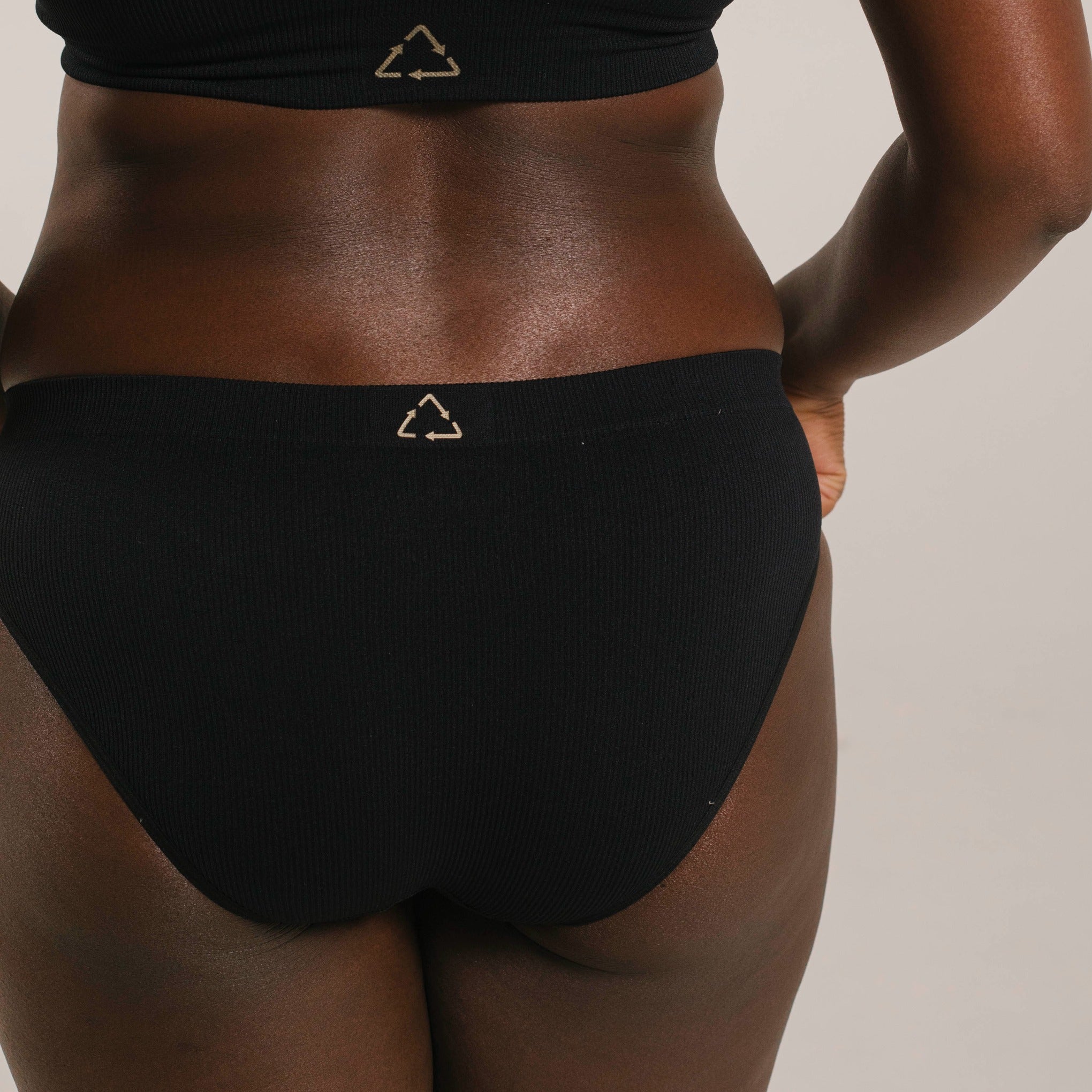 Ethically made recycled seam free black bikini brief by Underwear for Humanity: Flexible and comfortable, stretches across sizes. Models wear bikini brief underwear. Underwear is made from recycled nylon and sits low on the waist, full seat coverage and smooth on the body.