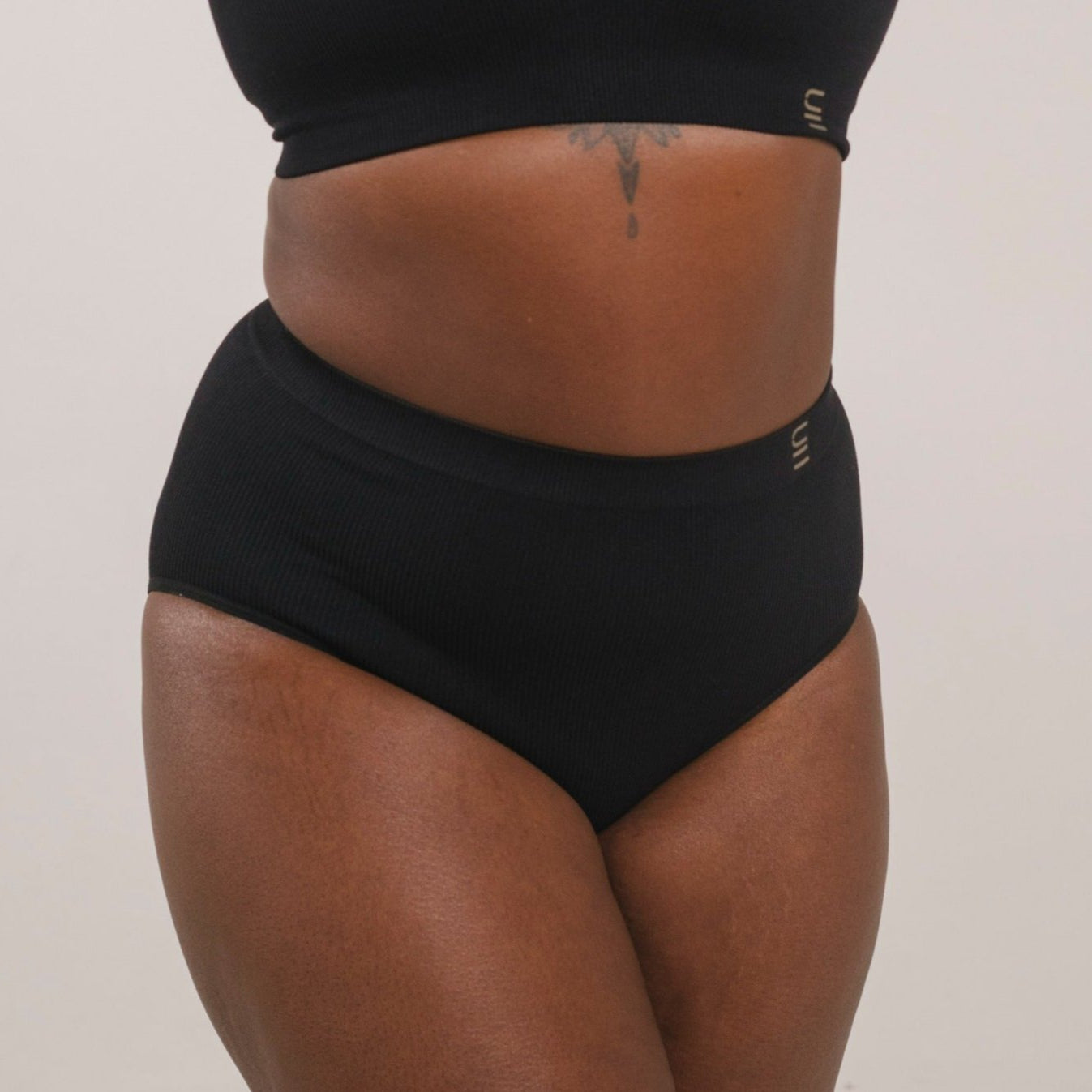 Sustainable, ethically produced black wireless bra by Underwear for Humanity. For DD-GG cup sizes. Recycled materials, flexible, supportive. Knitted bra and band, adjustable straps. Model wears the DD+ bra.