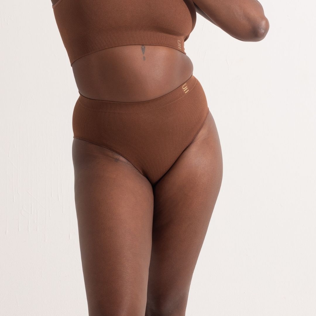 Sustainable, ethically made Nude 5- Medium Dark Skin tone high waist seam free g-string by Underwear for Humanity: Flexible and comfortable, stretches across sizes. Models wear high-waisted G -string underwear. Underwear sits high on the waist, high on the seat, and smooth on the body, made from recycled nylon.