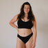 Ethically made recycled seam free black bikini brief by Underwear for Humanity: Flexible and comfortable, stretches across sizes. Models wear bikini brief underwear. Underwear is made from recycled nylon and sits low on the waist, full seat coverage and smooth on the body.