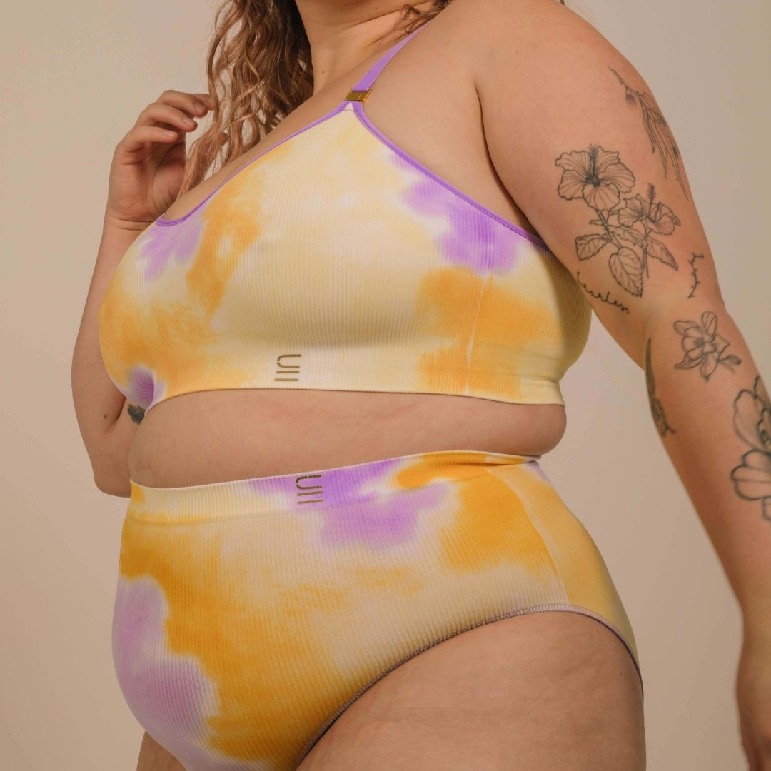 Sustainable sunrise yellow and purple tie dye seam free high waist brief by Underwear for Humanity: ethical, sustainable. sizes 6-26. light, breathable, stretches across sizes. Models wear high-waisted underwear. underwear sits high on the waist, full seat coverage, Seam free underwear. made from recycled nylon