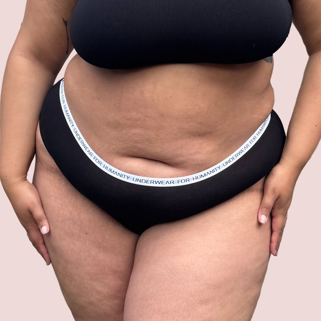 Underwear for Humanity, sustainable, organic and ethically made black cotton underwear.  Soft , breathable, Cheeky coverage, sits high on hips. Model wears Cheeky Cotton underwear in black with a white, recycled nylon elastic waist band.  