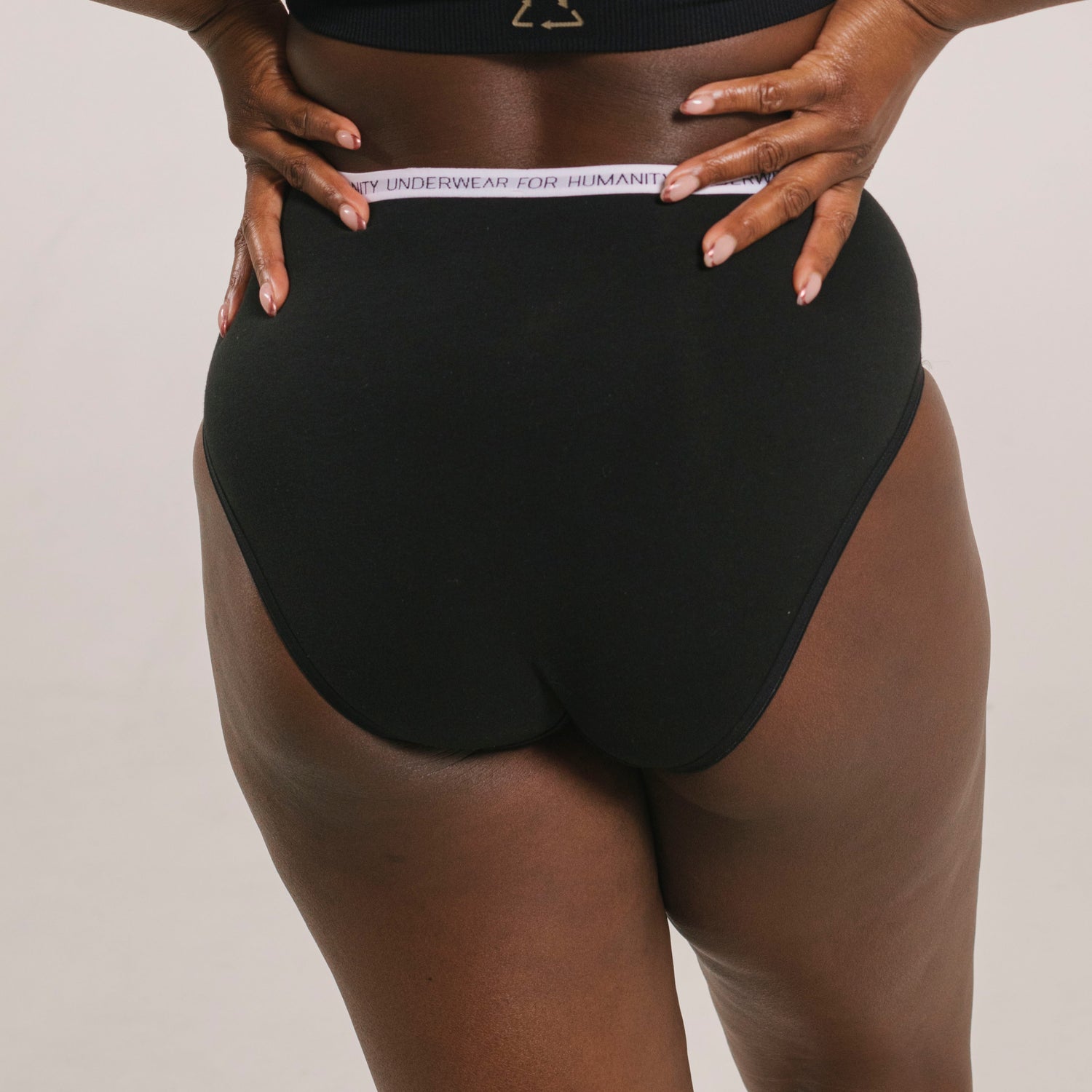 Underwear for Humanity, sustainable, organic and ethically made black cotton underwear.  Soft , breathable, full coverage, sits high on waist. Model wears High waisted Cotton underwear in black with a white, recycled nylon elastic waist band.  