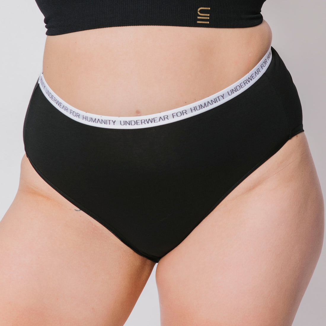 Underwear for Humanity, sustainable, organic and ethically made black cotton underwear. Soft , breathable, full coverage, sits high on waist. Model wears High waisted Cotton underwear in black with a white, recycled nylon elastic waist band.