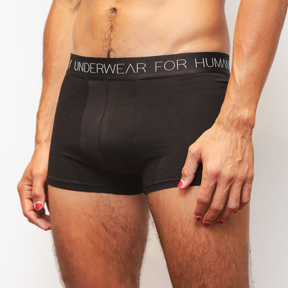 Sustainable, ethically made black trunk style underwear. Long leg, wide thigh fit with elastic bind, no riding, cup support close to the body. made with organic fabric and recycled elastic, thin, no dig waist band. Model wears shorts