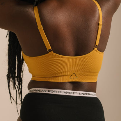 Sustainable, ethically produced gold wireless bra by Underwear for Humanity. For DD-GG cup sizes. Recycled materials, flexible, supportive. Knitted bra and band, adjustable straps. Model wears the DD+ bra.