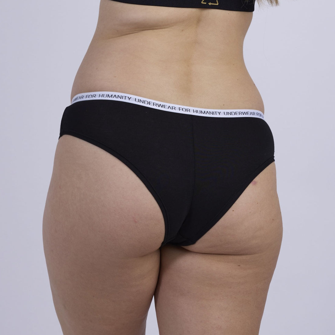 Underwear for Humanity, sustainable, organic and ethically made black cotton underwear.  Soft , breathable, Cheeky coverage, sits high on hips. Model wears Cheeky Cotton underwear in black with a white, recycled nylon elastic waist band.  