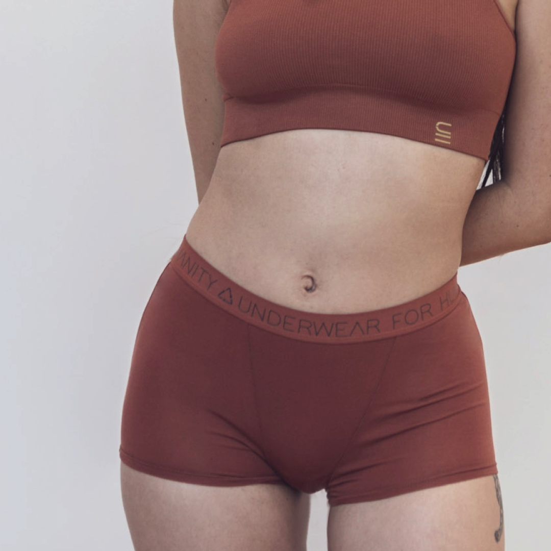 Sustainable, ethically produced clay shorts by Underwear for Humanity. Mid-rise, full coverage seat, thin, no-dig, elastic waist, short length sits higher on the leg. Made from sustainable tencel and recycled elastic. Models wear the shorts. 
