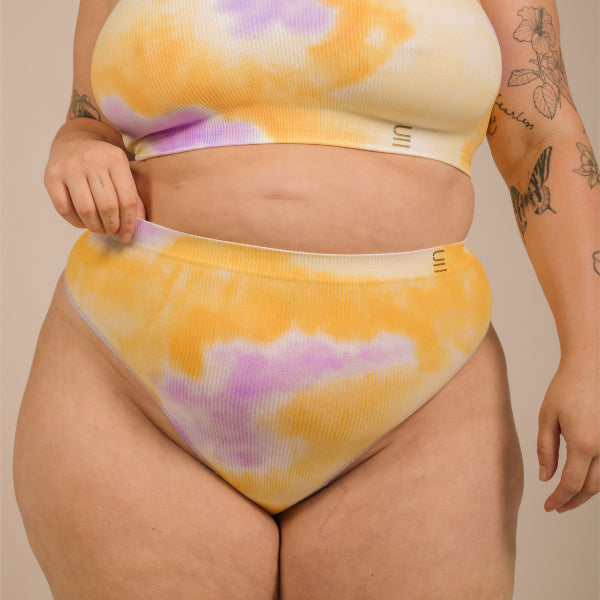 Sustainable, ethically made sunrise - yellow, orange and purple tie dye high waist seam free g-string by Underwear for Humanity: Flexible and comfortable, stretches across sizes. Models wear high-waisted G -string underwear. Underwear sits high on the waist, high on the seat, and smooth on the body, made from recycled nylon. 