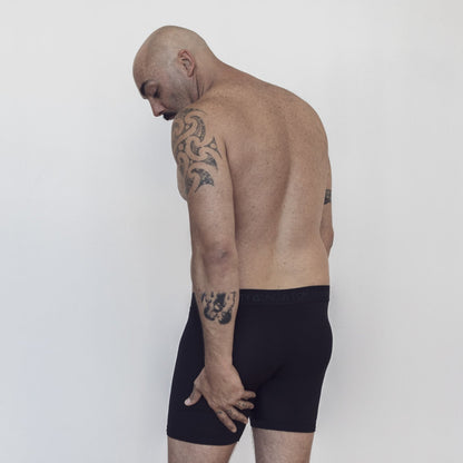 Sustainable, ethically made black trunk style underwear. Long leg, wide thigh fit with elastic bind, no riding, cup support close to the body. made with tencel fabric and recycled elastic, thin, no dig waist band. Model wears shorts